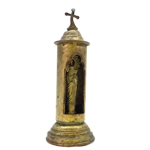 May include: A vintage brass religious shrine with a cross on top. The shrine has a cylindrical body with a small arched window revealing a statue. The base is round and tiered. The brass has a tarnished, aged appearance.