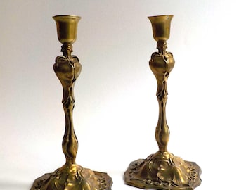 Könnte beinhalten: Zwei antike Messing-Kerzenständer mit aufwendigen floralen Designs. Die Kerzenständer haben einen ausgestellten Sockel und einen schlanken, geschwungenen Stiel. Die warmgoldene Farbe verleiht einen Hauch von Vintage-Charme. Dekorative Kerzenhalter.