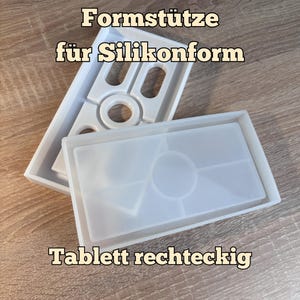 Könnte beinhalten: Eine weiße, rechteckige Formstütze für Silikonformen, kombiniert mit einer durchscheinenden, rechteckigen Silikonform für ein Tablett mit geometrischen Unterteilungen. Der Text Formstütze für Silikonform und Tablett rechteckig ist zu sehen.