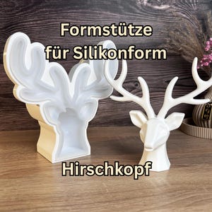 Könnte beinhalten: Eine weiße Formstütze für Silikonform Hirschkopf und eine fertige weiße Hirschkopf-Figur. Der Text Formstütze für Silikonform Hirschkopf ist sichtbar. Die Stütze dient dazu, die Silikonform während des Gießvorgangs in Form zu halten.