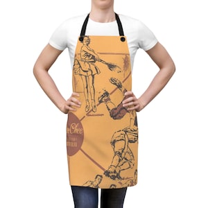 May include: An orange apron featuring a vintage-style graphic print of people playing tennis and football. The design includes a dark brown circular logo with the text 'Lee Chee' and 'All Season Portfolio' in a script and sans-serif font combination.