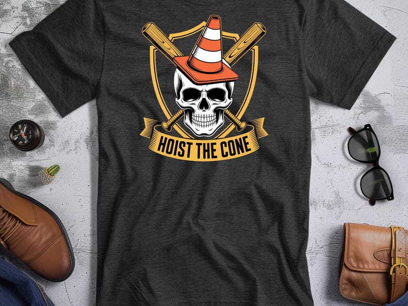May include: Dark gray t-shirt featuring a skull wearing an orange and white traffic cone, crossed baseball bats, and the text "HOIST THE CONE" in a banner. The design is set against a yellow shield.