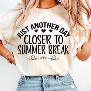 May include: A white t-shirt with the text "Just another day closer to summer break" in black lettering. Three small black hearts are above the word "closer".