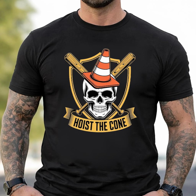 May include: Black t-shirt featuring a skull wearing an orange traffic cone, with crossed baseball bats behind it. The design includes a gold shield and banner with the text "HOIST THE CONE".