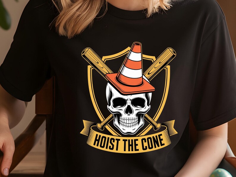 May include: Black t-shirt featuring a graphic of a skull wearing an orange and white traffic cone, with crossed baseball bats behind it. The text "HOIST THE CONE" is displayed on a banner below the skull.