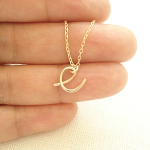 May include: A gold chain necklace with a delicate cursive letter 'E' pendant.