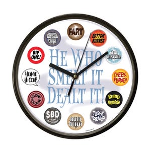 May include: A round wall clock with a black frame and a white face. The clock features the phrase "HE WHO SMELT IT DEALT IT!" in blue text. Various humorous terms like "FART" and "BOTTOM BURNER" are displayed around the clock face.