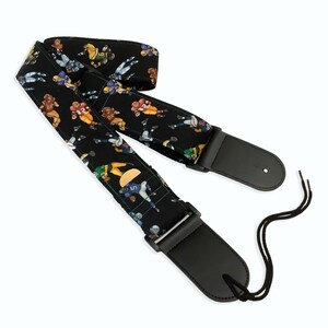 May include: Black guitar strap with a pattern of football players in various poses. The strap has black leather ends with adjustable straps.