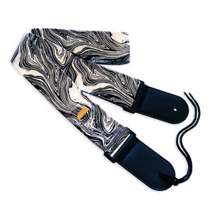 May include: Black and white guitar strap with a marbled pattern. The strap has black leather ends with adjustable straps.