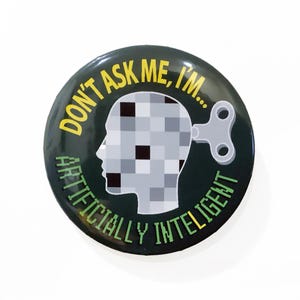 May include: A round green button with the text "Don't ask me, I'm... Artificially Intelligent" in yellow and green lettering. A cartoon head with a pixelated face and a wind-up key is in the center.