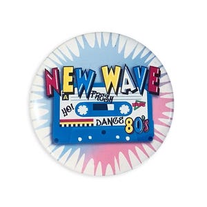 May include: A round button with a retro 80s theme. The button features the words "NEW WAVE" in colorful block letters above a blue cassette tape graphic. The tape has the words "Yo! Trash Dance 80's" printed on it, with a blue, pink, and white background.