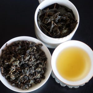 May include: Three white bowls, one containing loose leaf tea, one containing dried tea leaves, and one containing a light yellow tea.