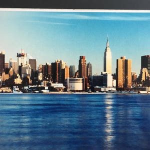 May include: A photograph of the New York City skyline with the Empire State Building in the centre. The buildings are reflected in the water in the foreground.