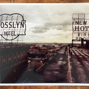 Può includere: Una fotografia in bianco e nero di un tetto con due grandi cartelli. Il cartello a sinistra dice "Rosslyn Hotel" e il cartello a destra dice "New Manhattan Hotel Fireproof".