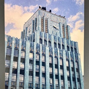 Può includere: Cartolina vintage raffigurante un edificio in stile Art Déco con una facciata blu-verde. L'edificio presenta numerose finestre ed elementi decorativi, con la scritta "Eastern" visibile in alto. È visibile anche un orologio.