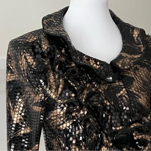 May include: A black and brown patterned jacket with a ruffled collar. The jacket has a snakeskin-like pattern with a shiny, textured appearance. The collar is a darker shade of black, and the jacket appears to be made of a luxurious material.