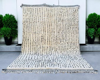 May include: A white and black Moroccan rug with a geometric pattern. The rug has a fringe border and is made of wool.