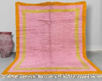 May include: A pink and orange rug with a fringe border. The rug has a double border with a yellow inner border and an orange outer border.