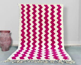 May include: A pink and white chevron patterned rug with fringe on the ends. The rug is made of a soft, fluffy material.