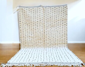May include: A white rug with a black polka dot pattern. The rug has a fringe border and is made of a soft, fluffy material.