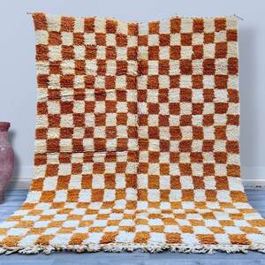 May include: A large, rectangular, checkered rug with a white and orange color scheme. The rug has a fluffy texture and a fringe border.