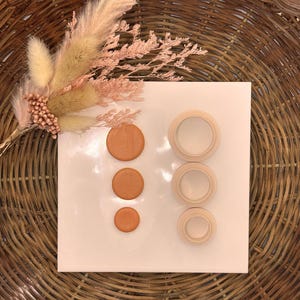 May include: A set of four terracotta-coloured round buttons and three wooden rings in various sizes. The buttons and rings are arranged on a white surface.