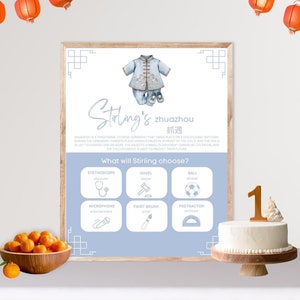 May include: A blue and white illustrated poster with the text "Stirling's zhuazhou 抓週" and a picture of a baby wearing a traditional Chinese outfit. The poster has a list of items with the text "What will Stirling choose?" and includes a stethoscope, a saw, a ball, a microphone, a paintbrush, and a protractor.