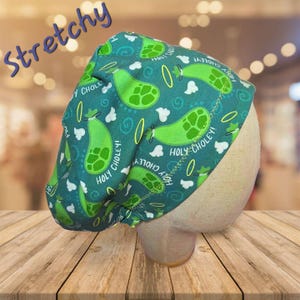 May include: A teal surgical scrub cap with a pattern of green pickles, white clouds, and yellow rings. The words "HOLY CHOLEY!" are printed on the cap. The word "Stretchy" is written in purple script.