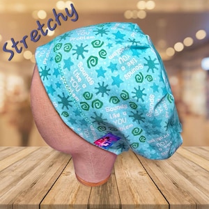 May include: A light blue, patterned scrub cap with the text "Sounds Like a YOU Problem" and star and swirl designs. The word "Stretchy" is written in a cursive font across the top left of the cap. The cap is displayed on a mannequin head.