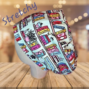 May include: A turquoise blue stretchy fabric headband with a print of a bookshelf filled with colorful books. The book titles include "Triggers Fairy Smut", "Fated Mates", "Morally Gray", "Banned", "Love Triangle", "|| Lust", "|| Love", "STFUATTDLAGG", "Spicy", and "Vibes".