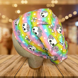 May include: A colorful skull cap featuring a repeating pattern of white skulls with pink roses, crossbones, and hearts on a rainbow background. The cap is made of soft fabric and is designed to fit comfortably.
