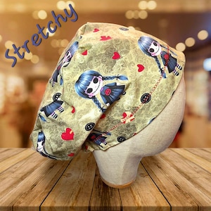 May include: A light green surgical scrub cap with a repeating pattern of a cartoon girl with blue hair, red hearts, and black buttons. The word "Stretchy" is written in blue script across the top.