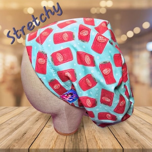 May include: A blue and red patterned scrub hat with the text "Dr Pepper" repeated on the fabric. The hat is stretchy and has a small blue tag with a design on it.