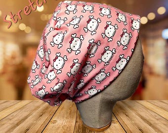 May include: Pink skull cap with a repeating pattern of white skulls with red bows. The word "Stretchy" is written in pink script across the top left of the image. The cap is displayed on a mannequin head.