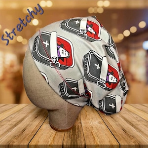 May include: A gray, stretchy cap with a repeating pattern of coffins, each containing a cartoon vampire. The coffins are black with white crosses and red interiors. The word "Stretchy" is written in blue script on the side.