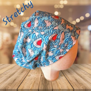 May include: A blue and white stretchy fabric hat with a shark and wave pattern. The hat is made of a soft, comfortable material and is perfect for everyday wear.