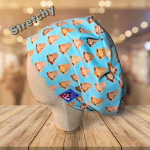 May include: A light blue, stretchy surgical scrub cap featuring a repeating pattern of brown and peach-colored nose illustrations. The word "Stretchy" is printed in brown across the top. A small, colorful patch is visible on the side.