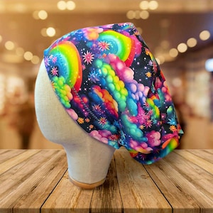 May include: A colorful head covering with a vibrant rainbow and cloud pattern. The fabric features a black background with rainbows, clouds, and star-like floral accents. The head covering is displayed on a mannequin head.