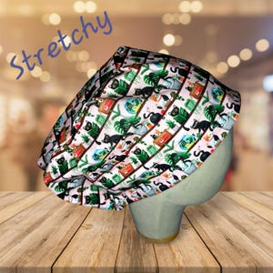 May include: A pink and white scrub hat with a repeating pattern of black cats, plants, and fish bowls. The text "Stretchy" is written in blue letters on the top left corner of the image.
