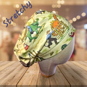 May include: A yellow and green stretchy scrub hat with a dinosaur and cowboy print. The hat has the word "Stretchy" written on it.