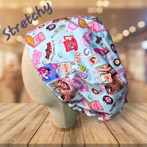 May include: A blue and pink patterned surgical scrub hat with a variety of images and text, including "Midwest Princess Chappel" and "Is it casual now?"