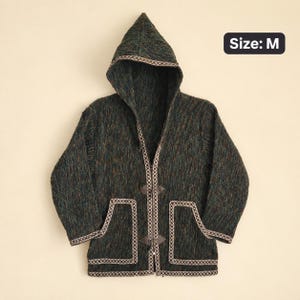 May include: A dark green hooded jacket with a textured finish, featuring long sleeves, two front pockets, and a front toggle closure. The edges of the hood, pockets, and hem are trimmed with a patterned beige and brown border. The text Size: M is visible.