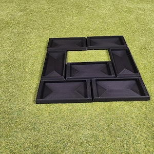 May include: Black, geometric-shaped trays arranged on a green surface. The trays are rectangular with angled sides, forming a square with a central opening. The arrangement suggests a puzzle or organizational system.