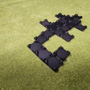 May include: Black interlocking foam floor tiles arranged in a geometric pattern on a green surface. The tiles have a textured surface and are designed to connect together. The overall shape resembles a stylized letter or symbol.