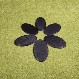 May include: Six black, oval-shaped objects arranged in a flower-like pattern on a green surface. Each object has a textured surface and a smooth, rounded edge. The objects are evenly spaced.