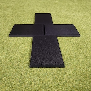 May include: A black, cross-shaped object composed of four rectangular pieces. The object is set against a green, textured background. The pieces appear to be made of a textured material.