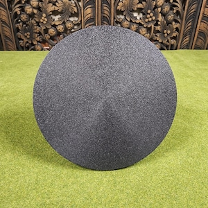 May include: A large, round, dark gray object with a textured surface. The object is centered on a green surface. The background features carved wooden panels.