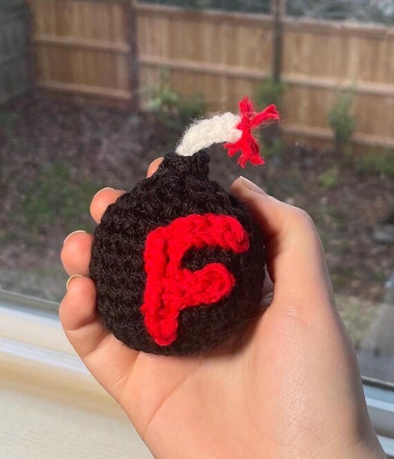 A hand-crocheted literal 'F-bomb' — a yarn grenade that doubles as a stress toy and desk statement piece.