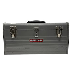 May include: A gray metal Craftsman toolbox with a black handle and silver latches. The toolbox has a red and white Craftsman logo on the front. The toolbox is rectangular and has horizontal ridges.