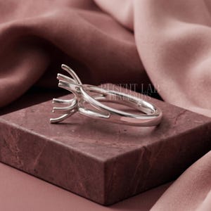 May include: A silver ring setting featuring a high, multi-prong head designed to hold a gemstone. The band is smooth and polished, with the text REGENT LAB DIAMONDS visible in the background. The metal has a reflective, metallic finish.